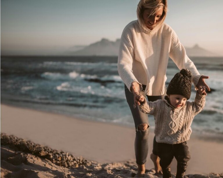 Mother helping her young child walk along a beach